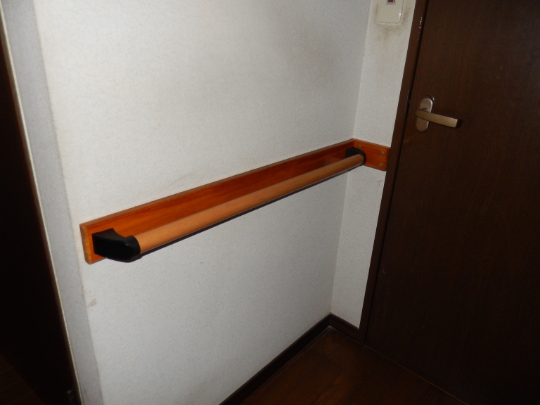 トイレ入口扉前に木製手すりを取付。